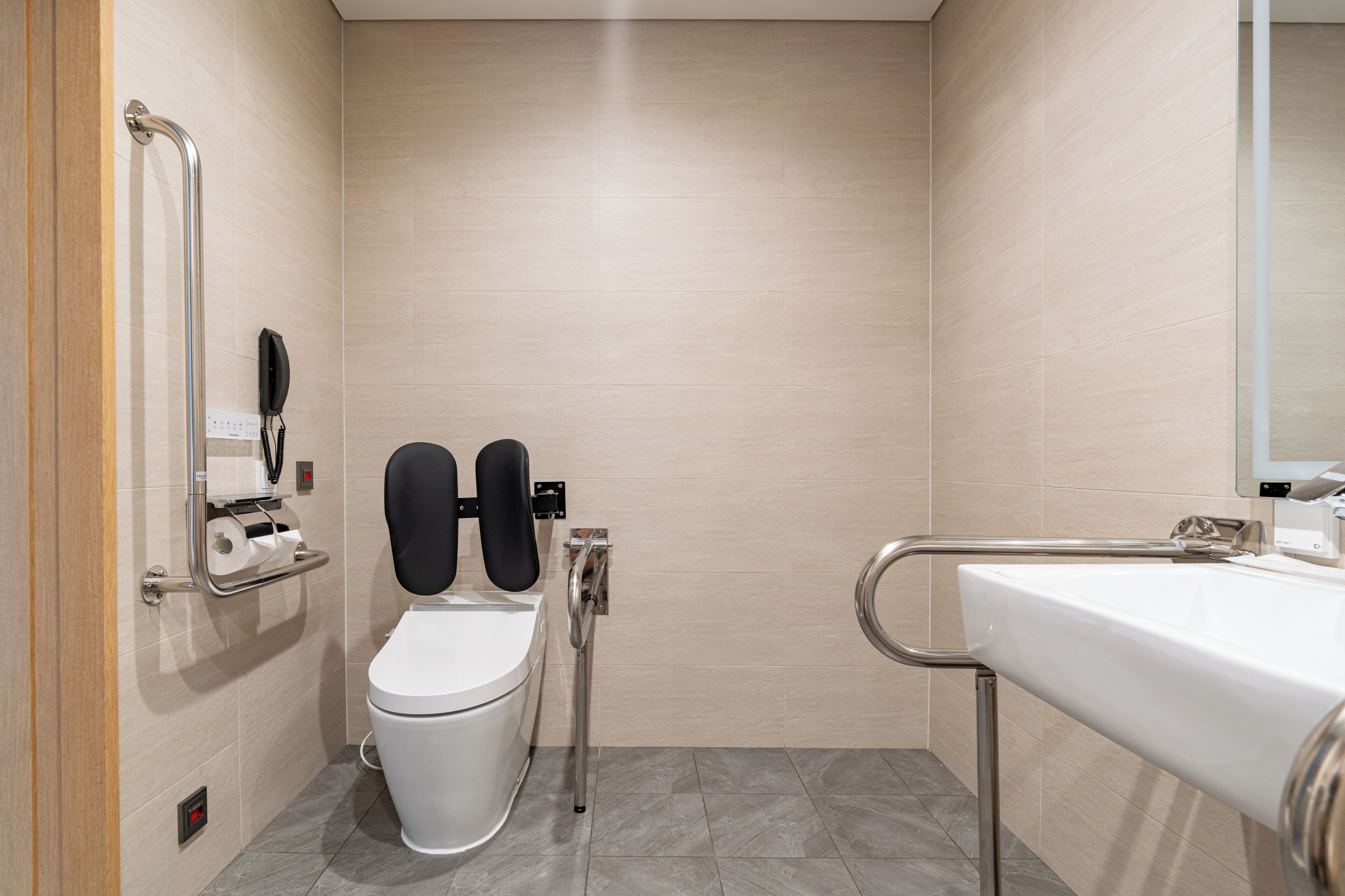 A modern bathroom with a white toilet, a handrail, a sink, and a mirror.
