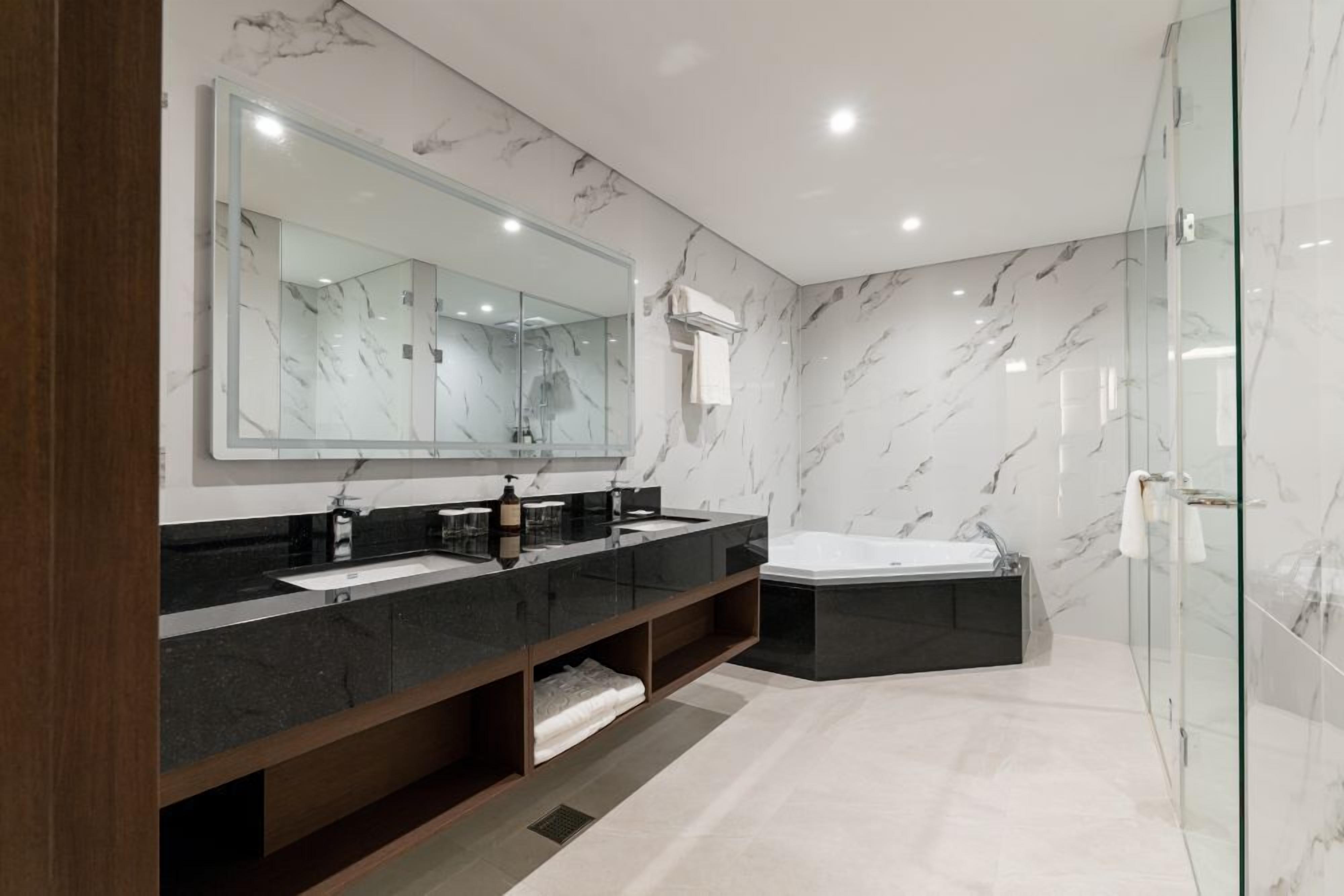Un baño moderno con un espejo grande, lavamanos dobles, una bañera y paredes de mármol.