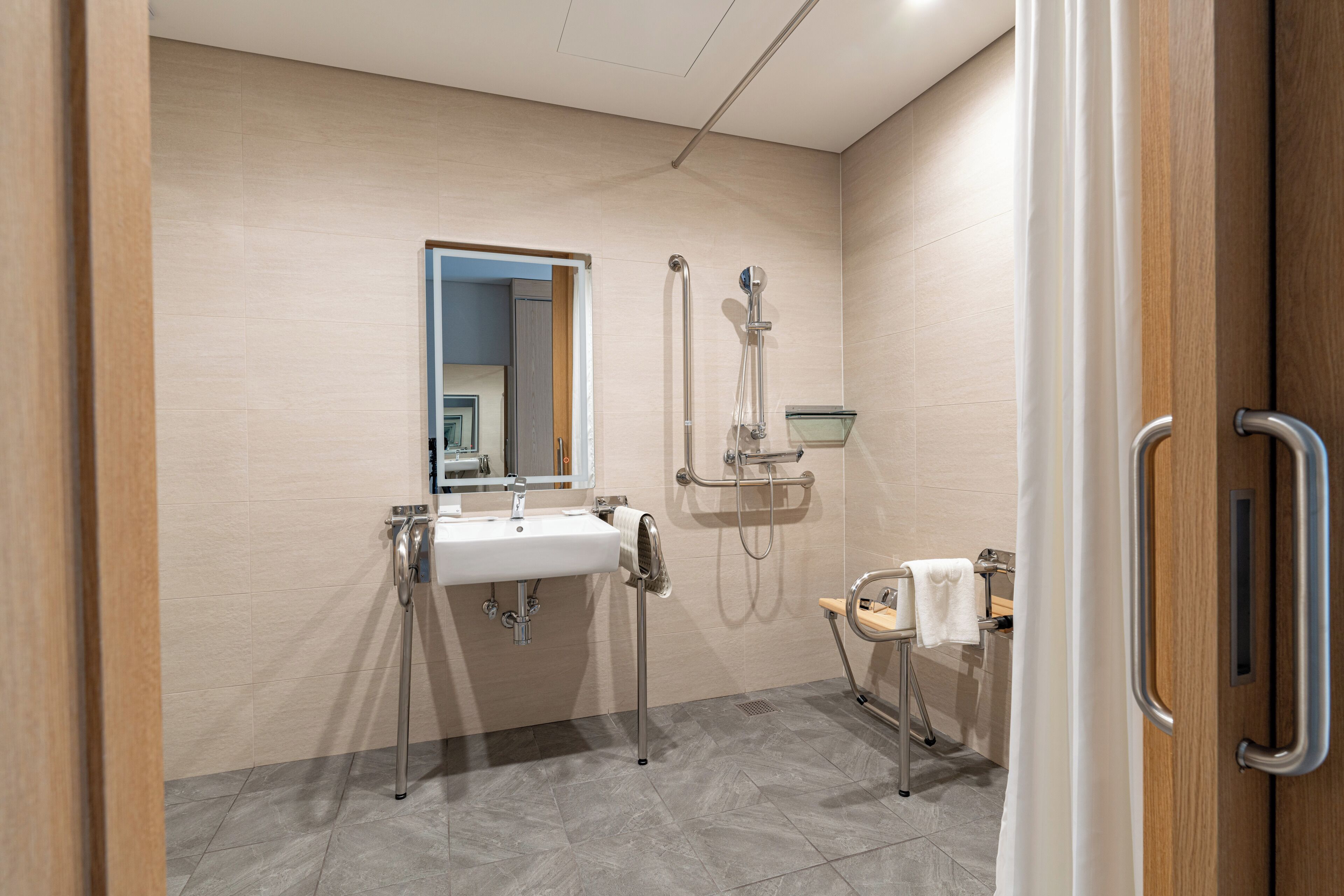Une salle de bain moderne équipée d’un lavabo, d’un miroir, d’une douche et de barres d’appui.
