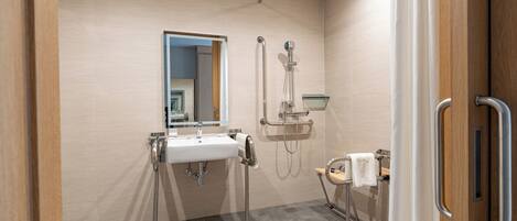 Une salle de bain moderne équipée d’un lavabo, d’un miroir, d’une douche et de barres d’appui.