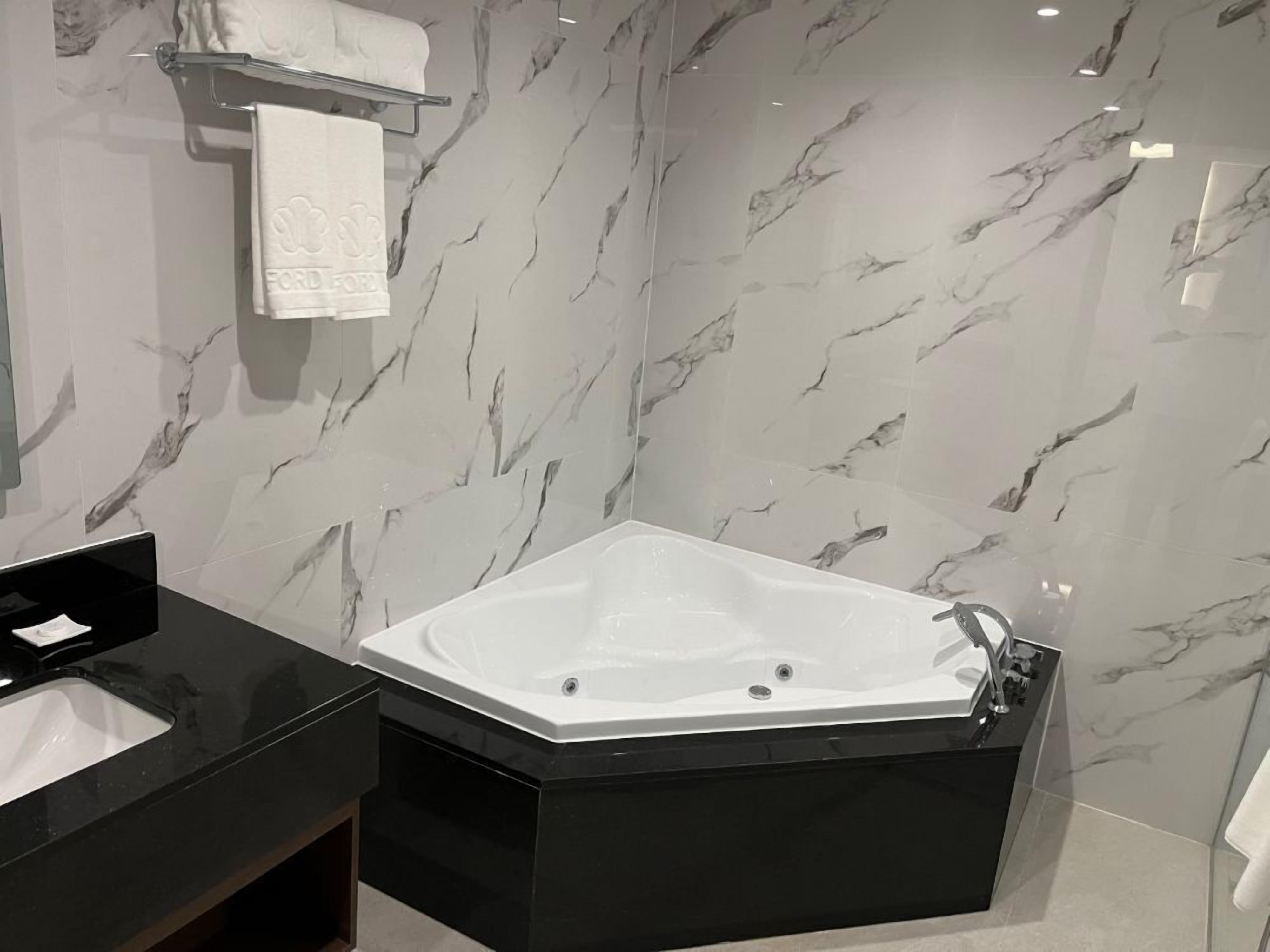 Un baño moderno con una bañera independiente grande, un tocador negro y paredes con diseño de mármol.