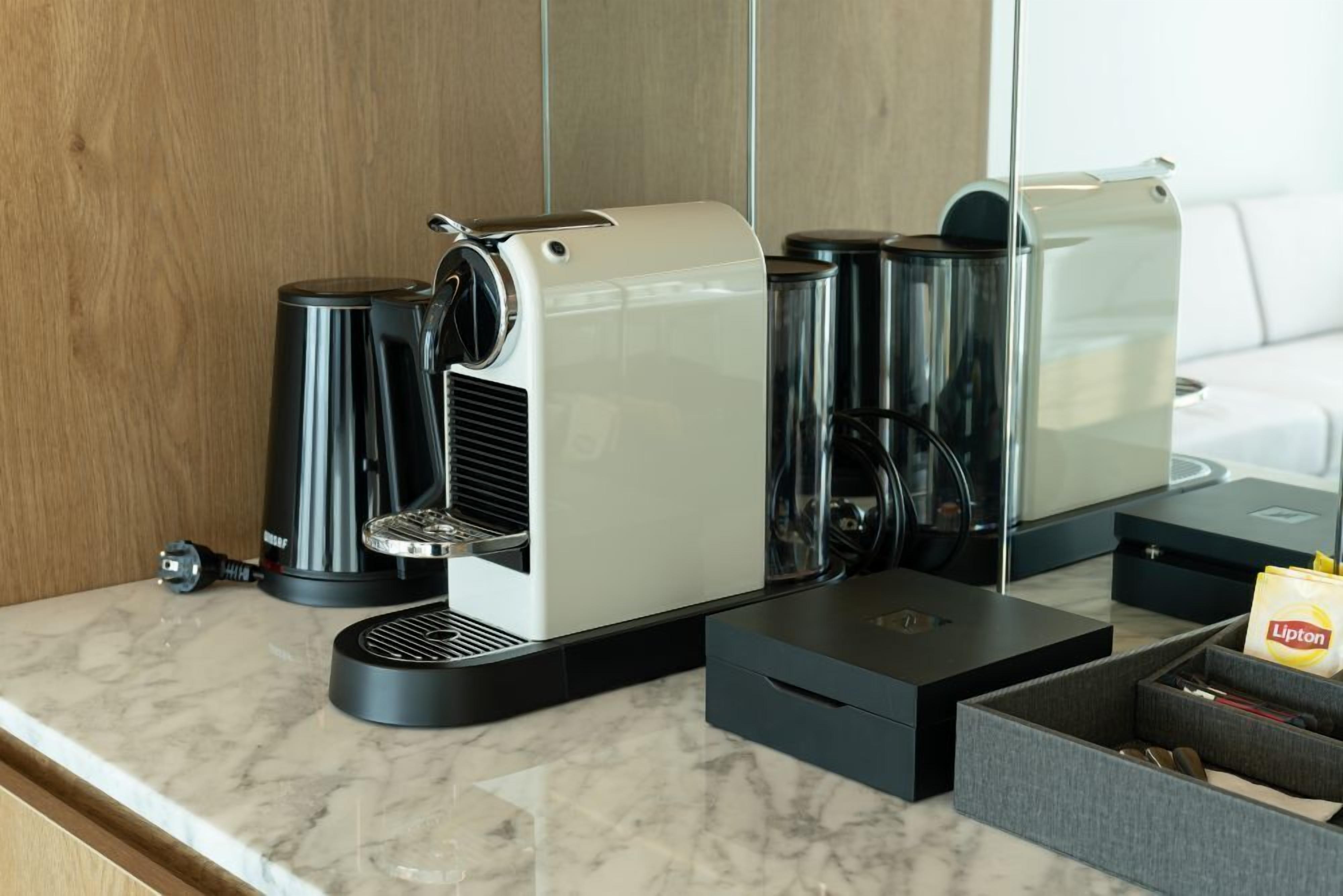 Una cafetera moderna sobre una encimera de mármol, con un molinillo de café, una bolsita de té Lipton y una caja de almacenamiento.