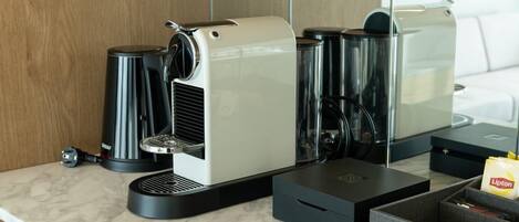 Una cafetera moderna sobre una encimera de mármol, con un molinillo de café, una bolsita de té Lipton y una caja de almacenamiento.