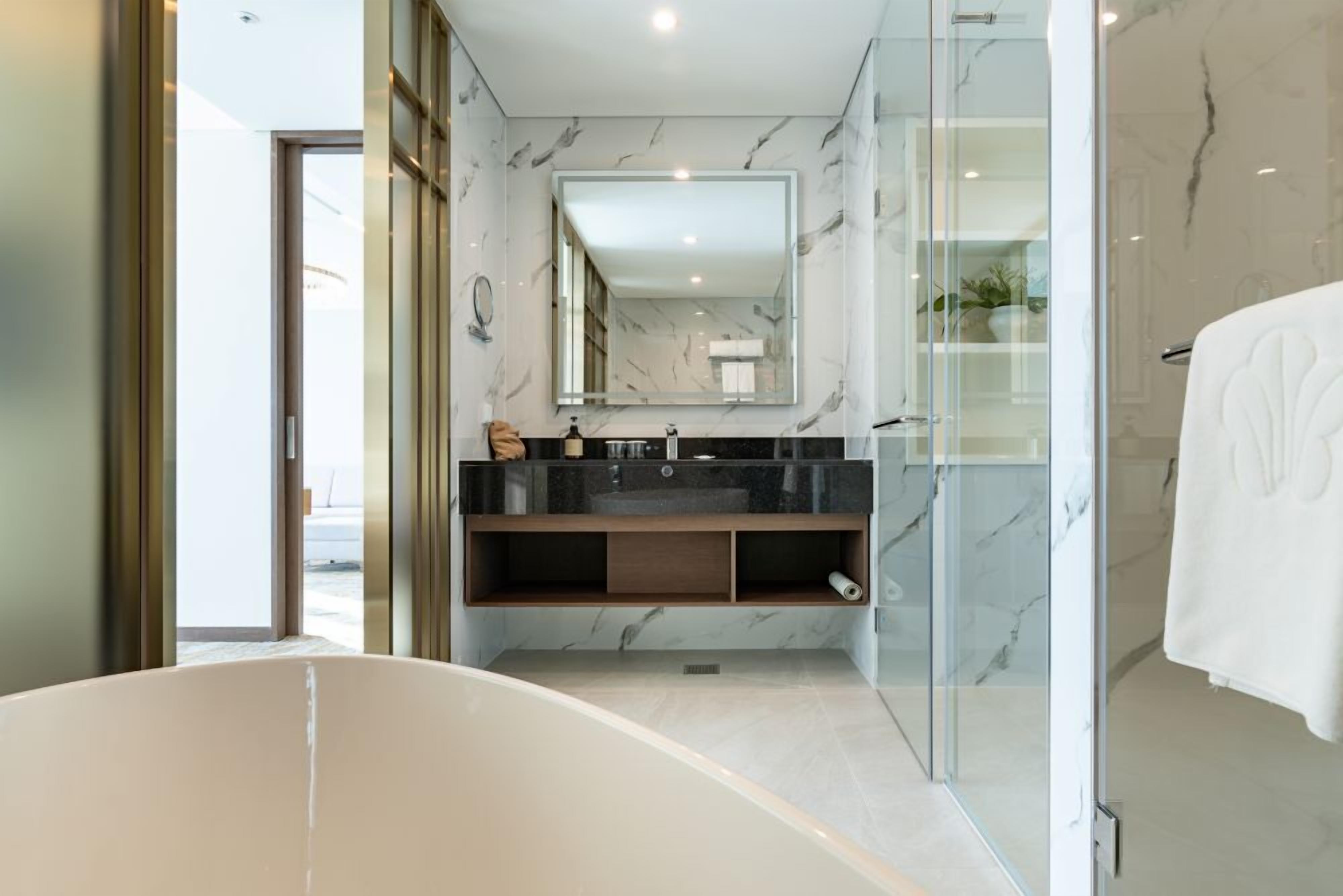 A modern bathroom with a freestanding bathtub, a glass-enclosed shower, and a marble backsplash.