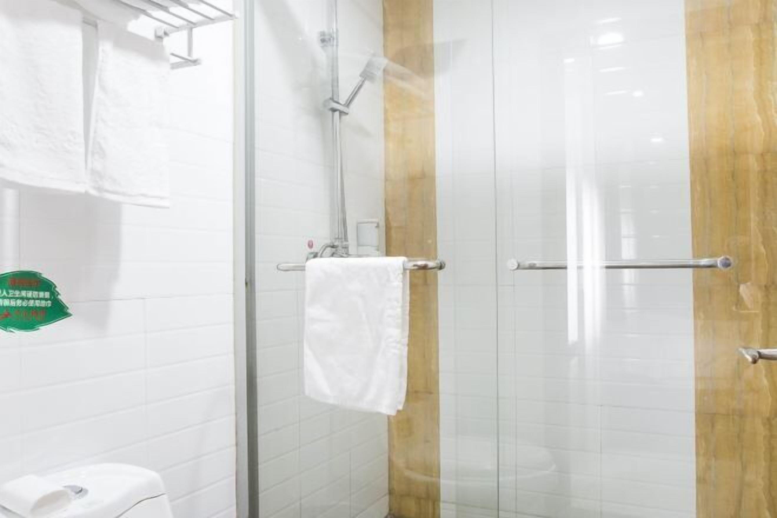 A bathroom with a glass shower enclosure, white tiled walls, and a wooden accent panel.