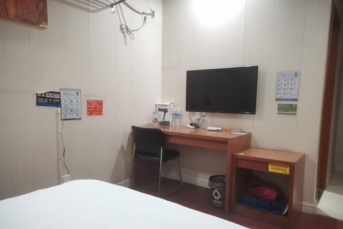 Ein Hotelzimmer mit einem Bett, einem Schreibtisch mit Stuhl, einem Fernseher und einer kleinen Mülltonne.