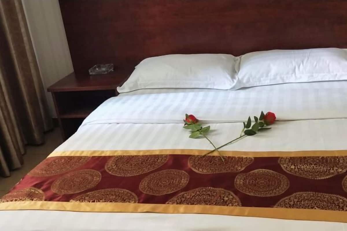 A hotel room with a neatly made bed, a wooden nightstand, and a decorative throw blanket.