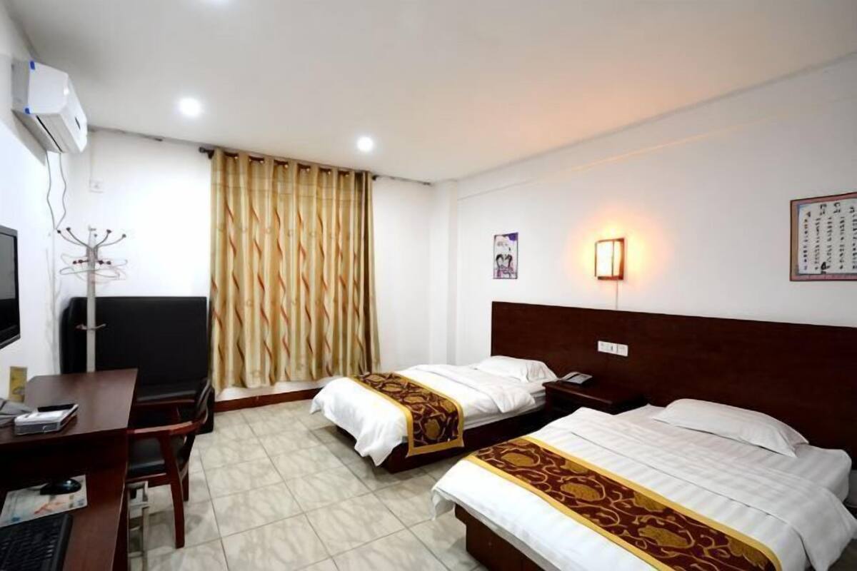 A hotel room with two beds, a desk, a chair, a television, and a curtain.