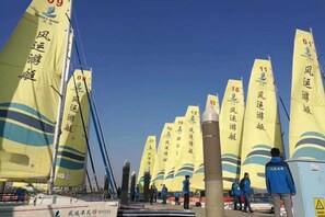 A row of sailboats with numbered sails, a clear sky, and people in blue jackets standing by the boats. - Beihai Jiajia Hotel (Beibuwan Square Branch) (Beihai)