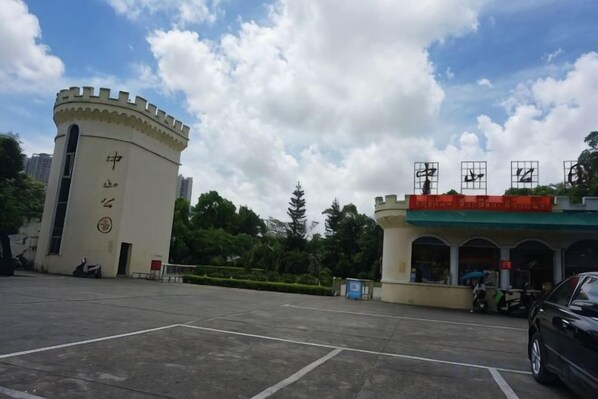 A parking lot with a building featuring a tower with inscriptions, a covered area with a red roof, and a clear sky. - Beihai Jiajia Hotel (Beibuwan Square Branch) (Beihai)