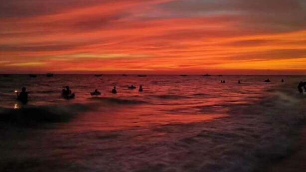 Tramonto sull'oceano con barche e persone in acqua.