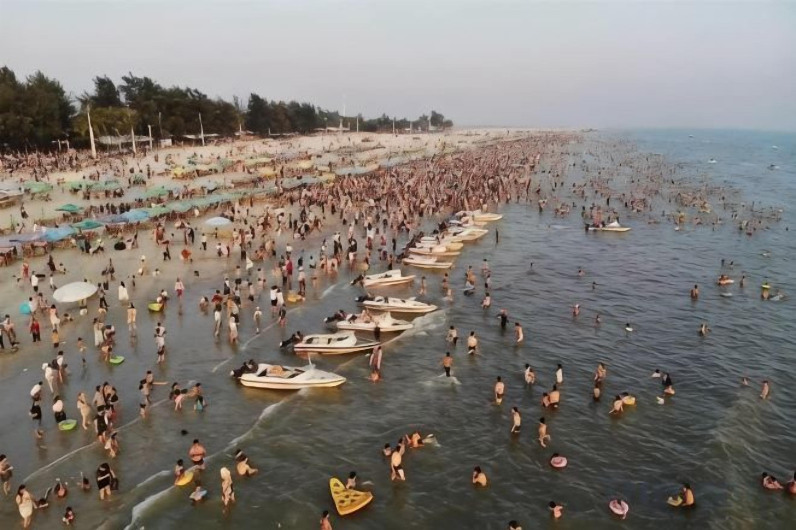 A crowded beach with numerous people and boats.