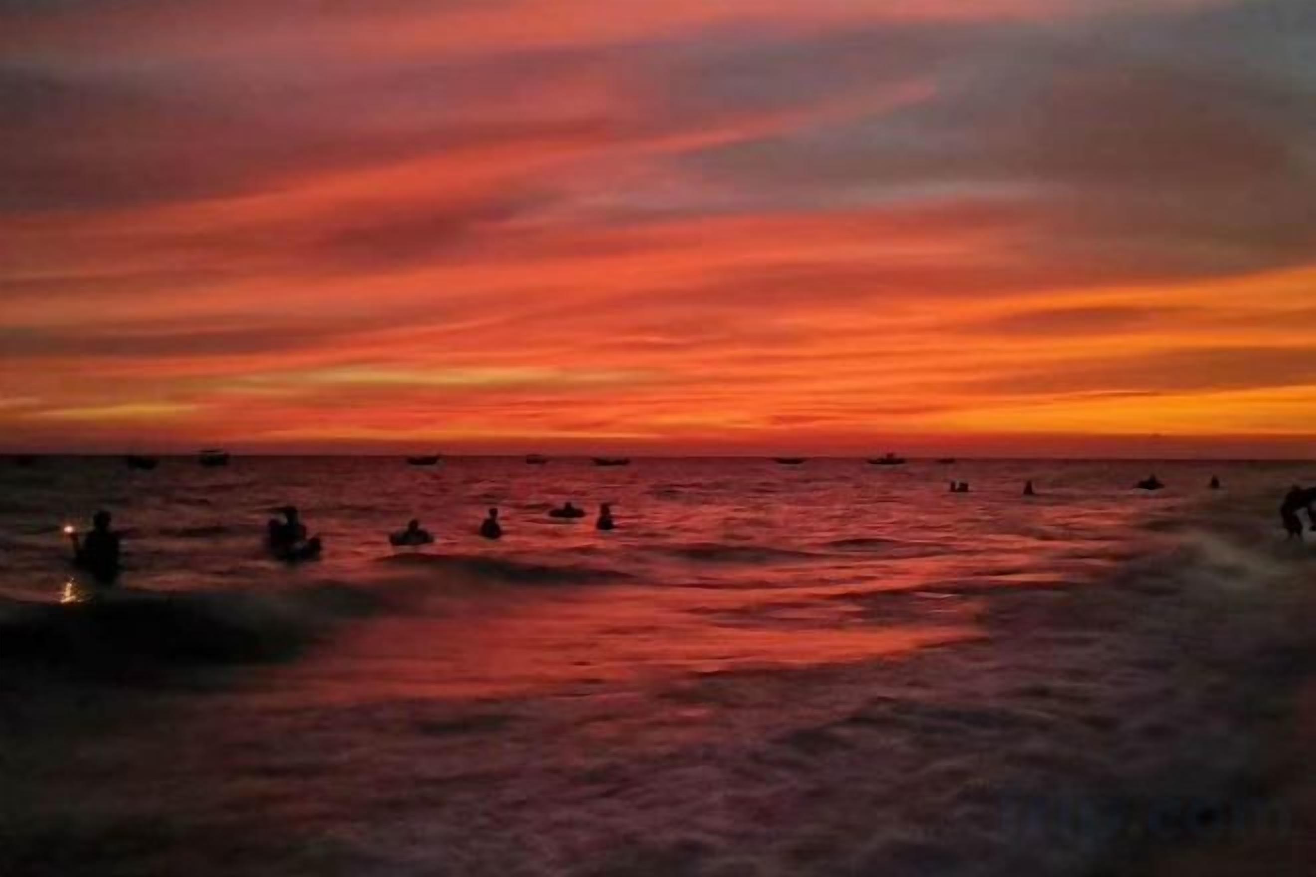 Un atardecer sobre el océano con barcos y gente en el agua.