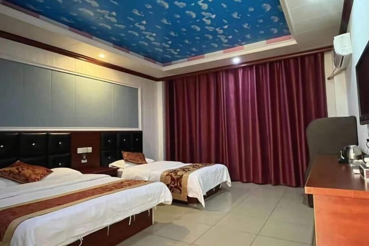 A hotel room with two beds, a desk, a TV, and a red curtain.