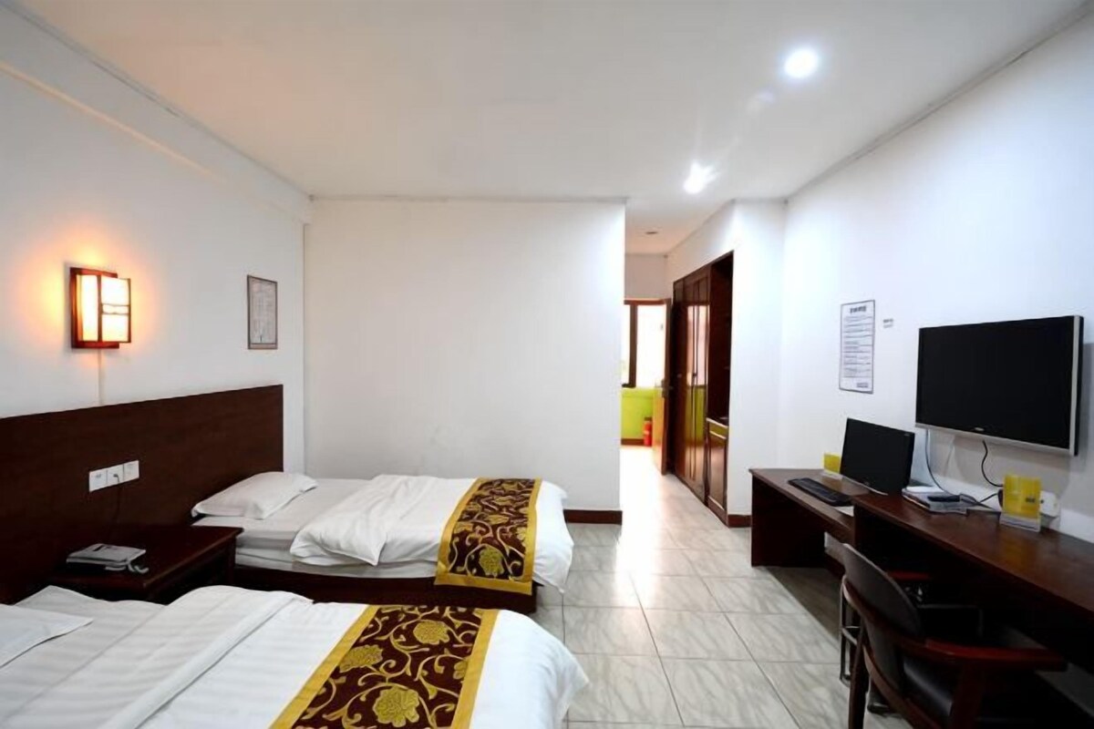 Habitación de hotel con dos camas, un escritorio, una silla, un televisor y una lámpara de pared.