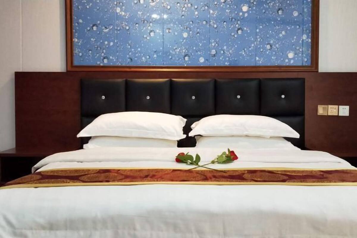 A neatly made bed with white linens and a decorative red and gold bedspread.