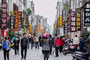Une rue animée, fréquentée par des piétons et des motocyclistes, bordée d’immeubles affichant des enseignes en chinois.