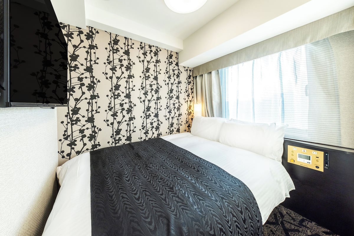 A hotel room with a bed, a control panel, and a window with curtains.
