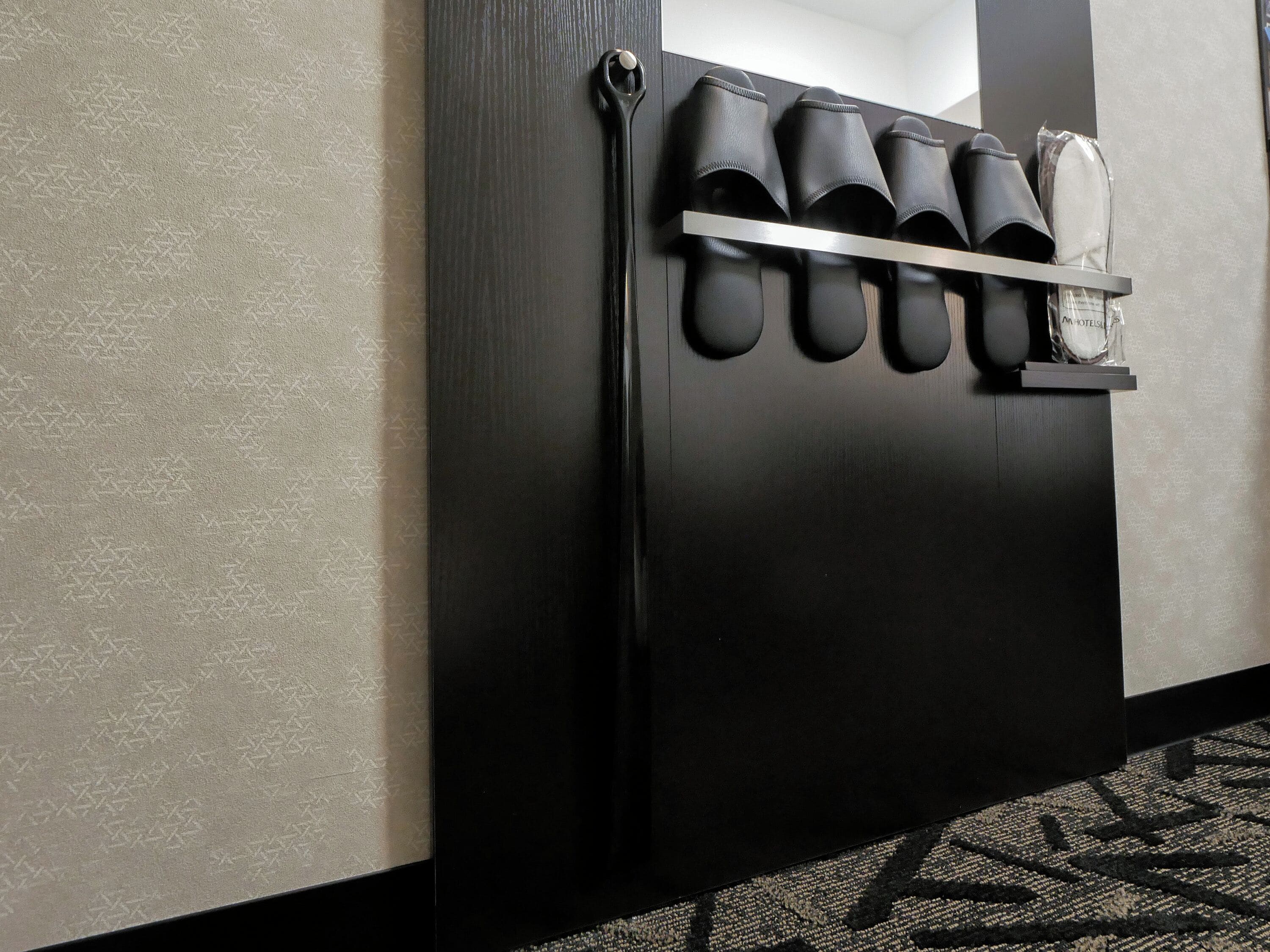 A black wall with a shoe rack holding several pairs of shoes.