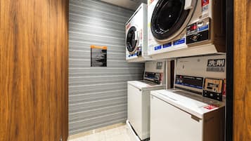 A compact laundry facility with a front-loading washer and dryer, a wall-mounted washing machine, and a tiled floor.
