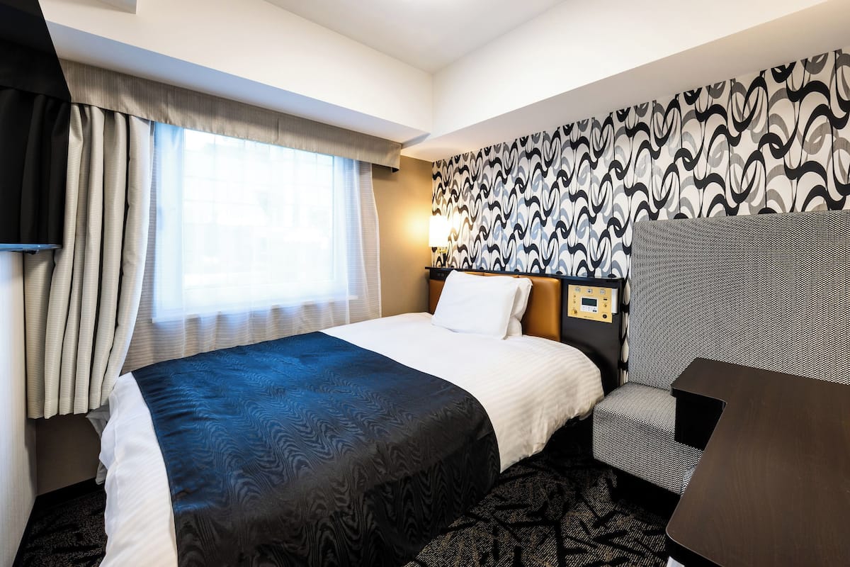 A hotel room with a bed, a desk, and a patterned wall.