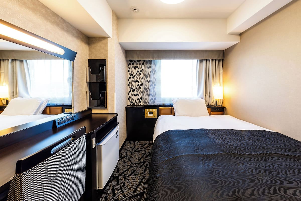 A hotel room with a bed, a desk, a chair, a wardrobe, and a mirror.