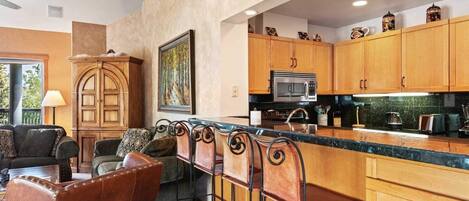 A modern kitchen with wooden cabinets, a central island with stools, a built-in microwave, and a large window.