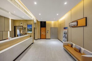 En hotellobby med en receptionsdisk, ett väntområde med en bänk och en dörr som leder till rummen.