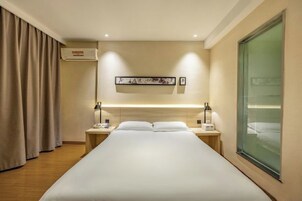 Habitación de hotel con cama, mesitas de noche, aire acondicionado fijado a la pared, una obra de arte enmarcada y un ventanal grande.