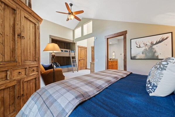 Une chambre avec un lit superposé, un ventilateur de plafond, une armoire en bois, un bureau et un tableau représentant un cerf.