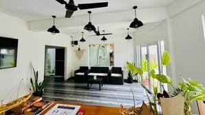 A spacious living area with multiple ceiling fans, a black sofa set, a wooden coffee table, and various potted plants. - Ramzu Villa (Thoddoo)