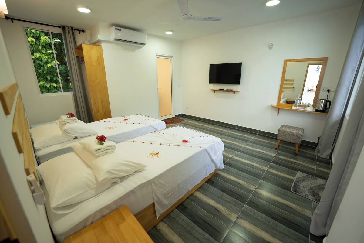 Ein Hotelzimmer mit zwei Betten, einem Fernseher, einem Spiegel und einem kleinen Hocker.