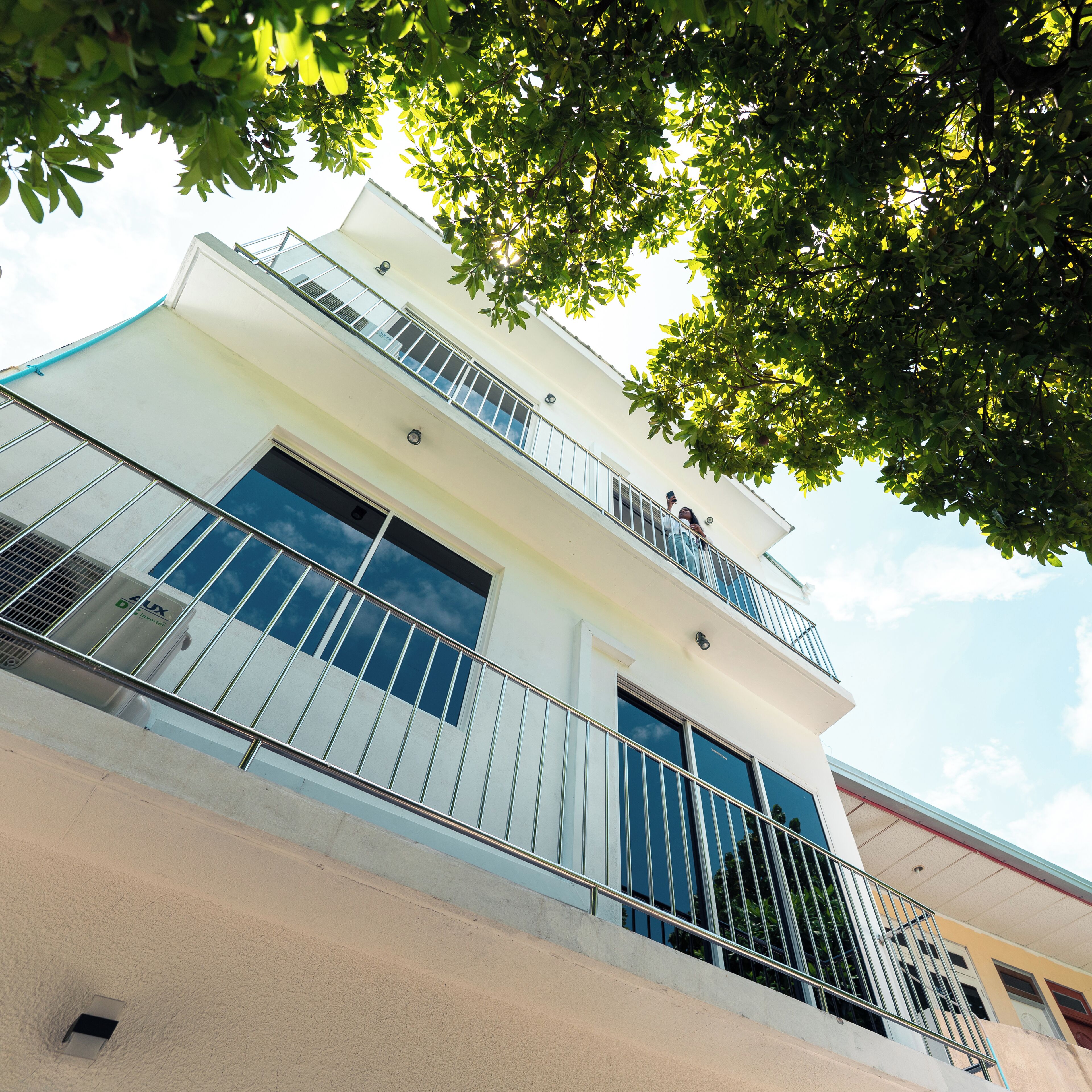 A multi-story building with a balcony on the second floor, large windows, and a visible air conditioning unit.