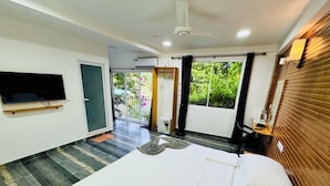 A modern hotel room with a large bed, a flat-screen TV mounted on the wall, and a balcony with a view of greenery. - Ramzu Villa (Thoddoo)