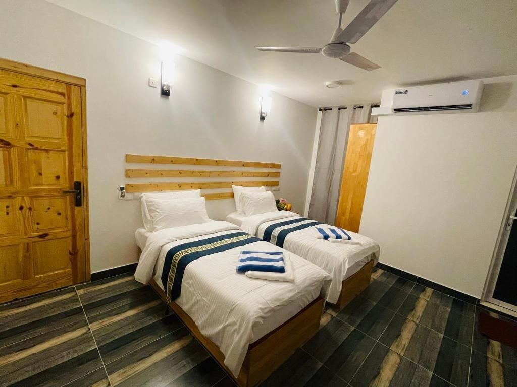 A hotel room with two beds, a wooden headboard, a ceiling fan, an air conditioning unit, and a striped floor.