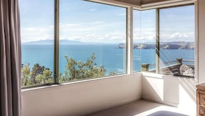 A room with large windows offering a view of the sea and distant mountains. - Seaview Sanctuary - Our Island (Waiheke Island)
