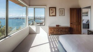 A bedroom with a large window offering a view of a coastal landscape. - Seaview Sanctuary - Our Island (Waiheke Island)