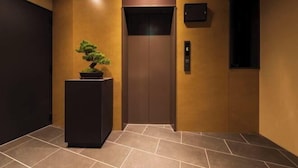 A modern elevator with a digital control panel, a potted plant, and a wall-mounted light fixture. - Shirakabanoyado - Ebisu (Osaka)