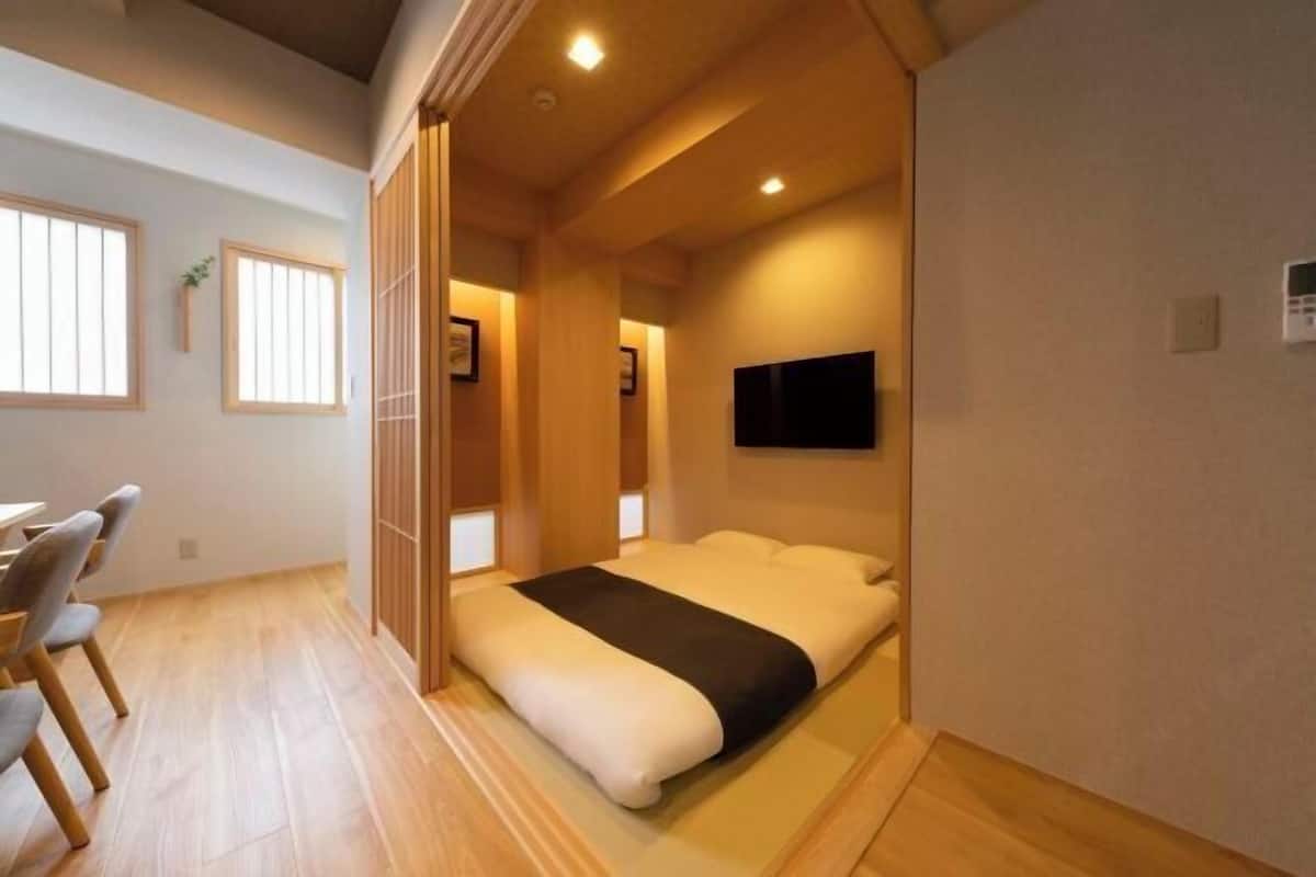 Habitació compacta amb llit, televisió penjada a la paret i zona de dinar amb caires.
