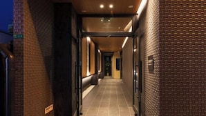 A corridor with tiled flooring and brick walls, leading to a door with a sign. - Shirakabanoyado - Ebisu (Osaka)