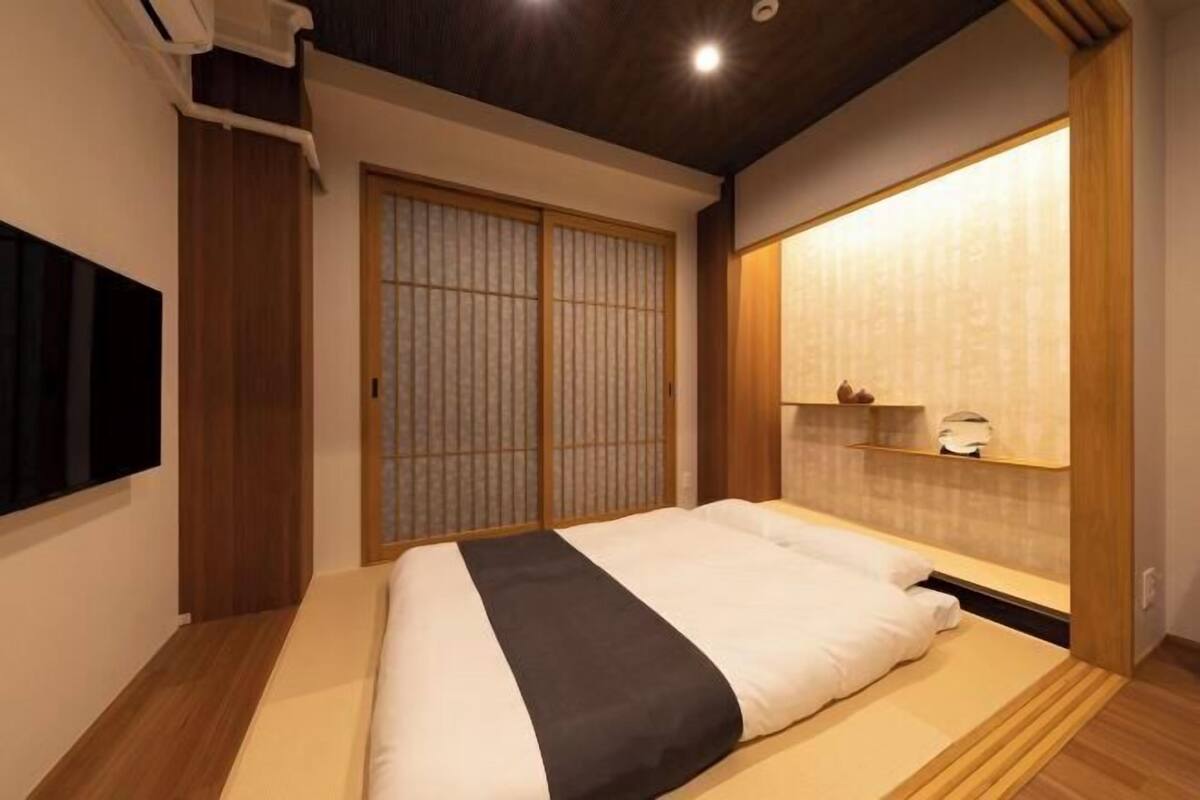 Habitació d'hotel acuradament ordenada amb un llit, portes corredisses, una estant amb objectes i una làmpada de paret.