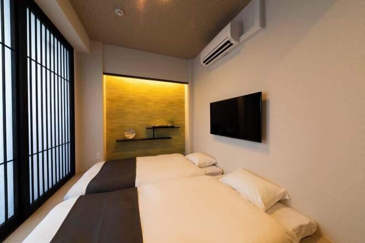 Habitació d'hotel amb dos llits, televisió penjada a la paret i una petita estant amb objectes decoratius.