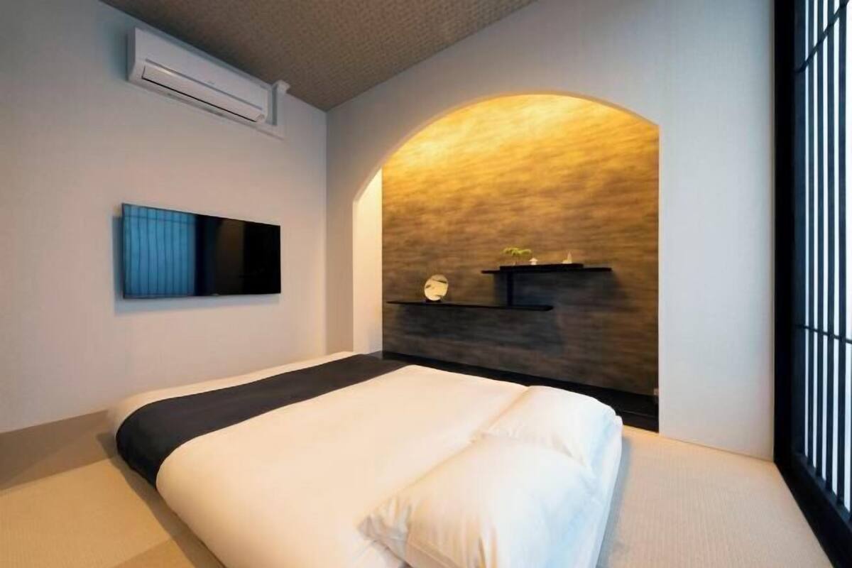 Habitació d'hotel moderna amb un llit gran, un televisor fixat a la paret, una prestatgeria integrada amb elements decoratius i un disseny de sostre allargat únic.