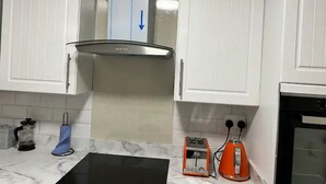 Una cocina con armarios blancos, encimera negra, cafetera de vidrio, tostadora naranja y horno negro.