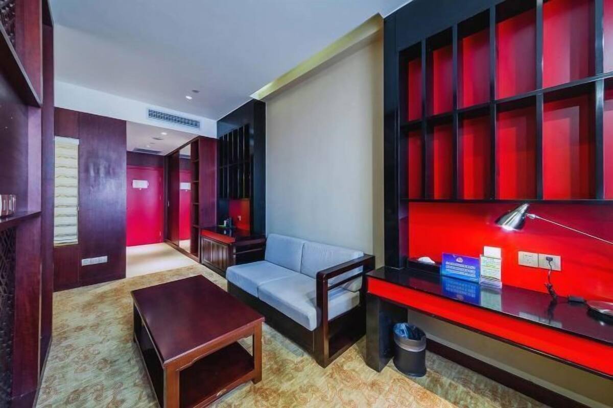 Habitació d'hotel moderna amb un sofà, una taula petita, un escriptori amb una làmpada i una paret vermella decorativa.