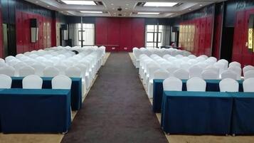 Une salle de conférence avec des rangées de chaises blanches, des nappes bleues et des murs rouges.