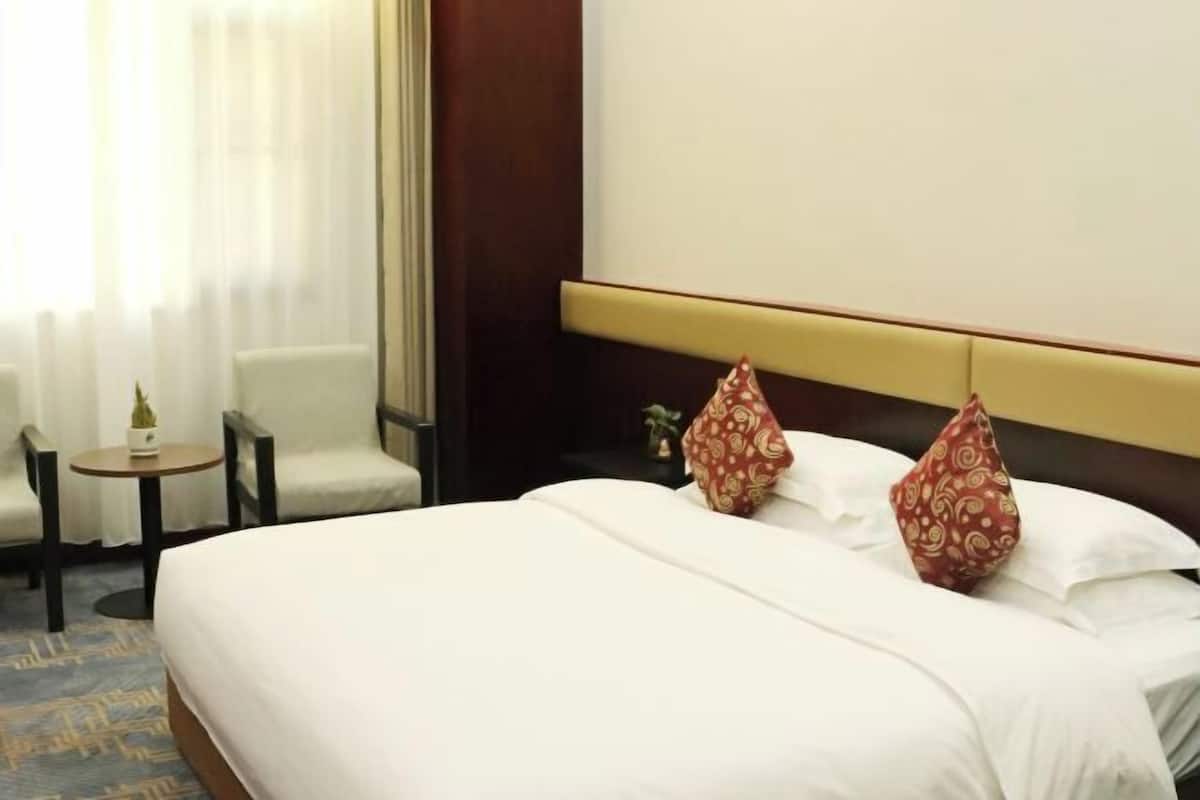 Habitació d'hotel amb un llit, dues cadires, una taula petita i una finestra amb cortines.