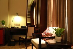 A cozy room with a desk, chair, and a sofa with a patterned cushion. There is a lamp on the desk and a potted plant on the sofa. - Guanjing Jiayuan Hotel (Beijing)