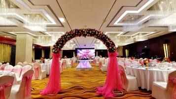 Une salle de banquet avec des tables rondes, une scène dotée d’un grand écran et une arche décorative.