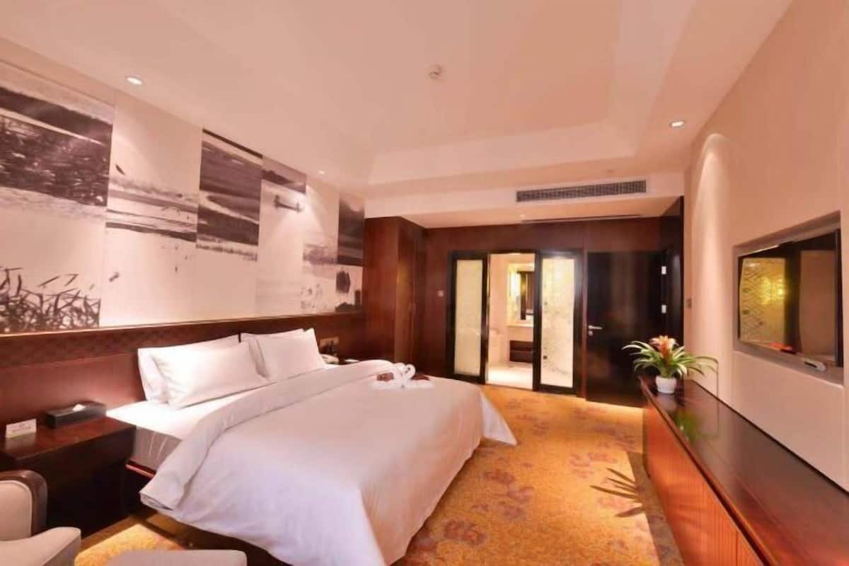 Habitació d'hotel amb un llit gran, una taula de treball, una cadira, un televisor i una paret amb obra d'art.